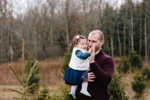 A family photo session with a family of three at a Christmas Tree Farm in Alto Michigan at Postema Christmas Tree Farm.