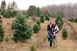 A family photo session with a family of three at a Christmas Tree Farm in Alto Michigan at Postema Christmas Tree Farm.