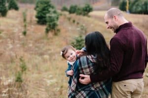 A family photo session with a family of three at a Christmas Tree Farm in Alto Michigan at Postema Christmas Tree Farm.