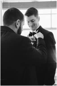 Black and White Photograph of groomsman helping the groom with his boutonnière.