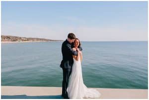 Bride and groom standing in front of the water with the Grand Haven shoreline in he background