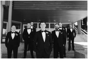 Black and white photography of groomsman staggered in front of a building in Grand Haven
