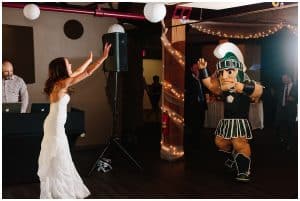 Bride throws her hands in the air when she is surprised by the Michigan State mascot joining her reception