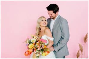 colorful wedding editorial shoot with a pink backdrop and bride and groom looking at each other lovingly
