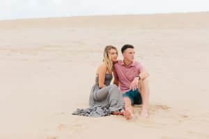 Couple sitting and looking off in the distance for their engagement photos at Silver Lake Sand Dunes