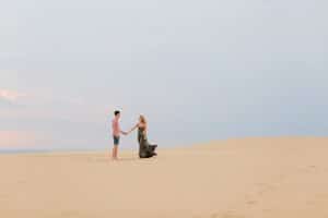 Couple standing on top of the dunes at Silver Lake for their summer time engagement phots. Girls' dress is flowing in the breeze.