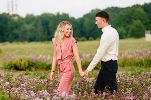 Couple walking and holding hands while looking at each other with love at Cherry Point Farms in a flower field