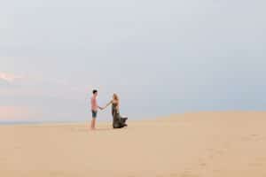 Couple standing on top of the dunes at Silver Lake for their summer time engagement phots. Girls' dress is flowing in the breeze.