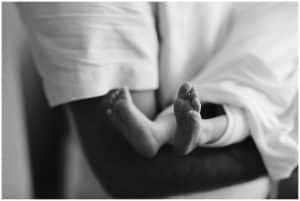 Black and white image of baby girl's feet as her father holds her in his arms.