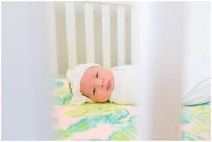 Newborn baby girl looks through her crib at the camera