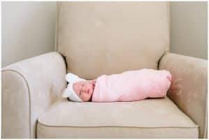 In home newborn session with baby girl laying on a rocker chair in a pink swaddle blanket