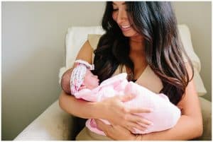 A mother holds her newborn baby girl and smiles as she looks down on her.