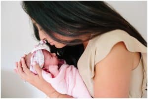 A mother leans in to kiss her newborn baby girl during an in home newborn photography session