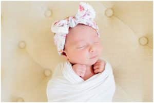 Newborn baby girl swaddled and laying on a chair while posed for a picture.
