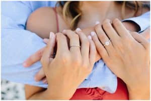 Close up of a girls engagement ring while her and her fiance wear bright summer colors.