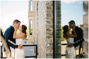 An engaged couple is standing on a fire escape and kissing while their reflection is mirrored in the background.