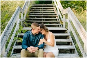 Engaged couple sitting on some stairs to the beach at Kirk Park while holding on to each others arms in a loving way.