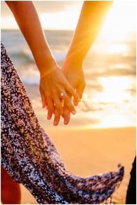Close up of a couple holding hands on the beach to show off the engagement ring.