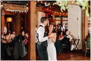 The bride and groom share a dance as a married couple and smile up at each other as their guests watch them.