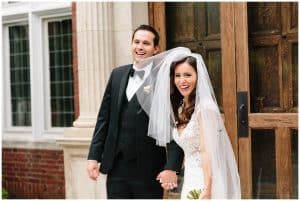 The bride and groom laugh while holding hands and standing in front of an hostoric building.