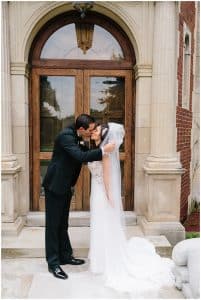 The bride and groom kiss in front of some old doors.