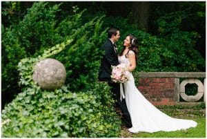 The bride and groom stand next to each other and almost hug as they look into each others eyes and smile.