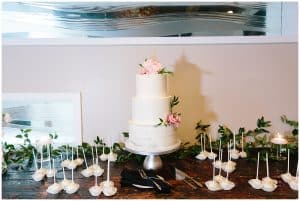 A picture of the wedding cake and some cake pops sitting on a table before the cake is cut.