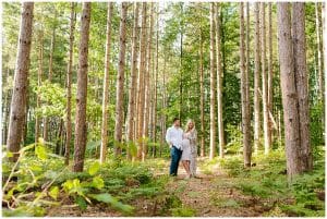 A couple stands in a forest near Riley Trails and poses for their maternity shoot.