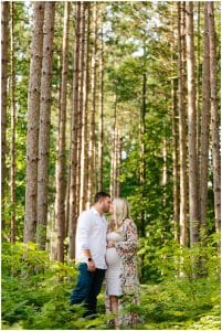A couple kissing under the trees in the woods near Riley Trails for their maternity photo shoot.