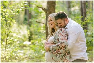 A maternity photo shoot with a couple laughing and smiling while in the woods at Riley Trails.