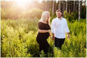 A couple laughs and walks through some greenery as they pose for some maternity photos taken by Mae Photo Co.