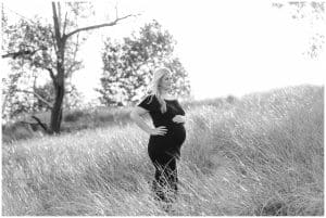 A black and white photo of a mother at Holland State Park as she holds her baby bump and looks off into the distance.