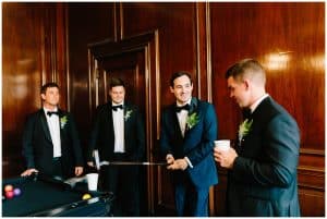 A photo of a groom and his groomsmen talking and getting ready outside of a room right before the wedding ceremony.