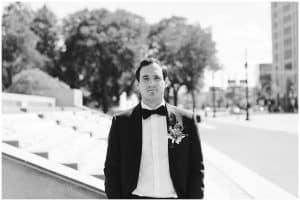 A black and white image of the groom standing outside and dressed in his suite right before his wedding.
