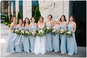 A bride and her bridesmaids posing for some wedding photos outside while putting their flowers on display.