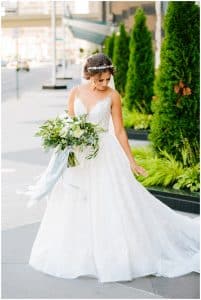 A bride stands outside and looks down at her dress as she posing for some wedding photos.