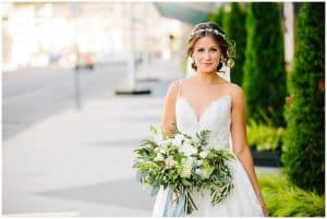 A bride smiles at the camera in a flowing sleeveless white wedding dress while standing outside for her wedding photos.
