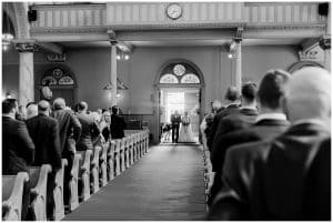 A black and white image of a bride standing with her father while he gives her away to her waiting husband.