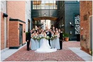 Photograph of a bridal party posing outside of a beautiful building with brick laid streets.
