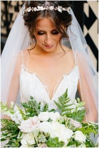 A close up picture of a bride on her wedding day; she is wearing her vail and looking down at her white and green flowers.