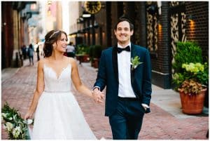 Bride and groom walking down a brick laid street while smiling, laughing, and holding hands right after their wedding ceremony.