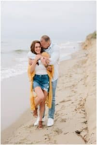 A soon to be groom grabs his bride from behind and kisses her forehead. The couple is engaged and at the beach in Holland.