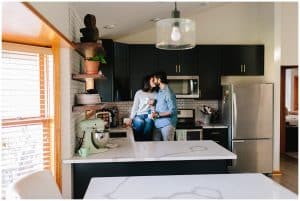 A young couple sitting on the kitchen counter of their newly remodeled home while kissing.