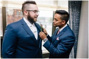 A photo of a groom getting assistance from one of his groomsmen as they prepare for the upcoming wedding ceremony.