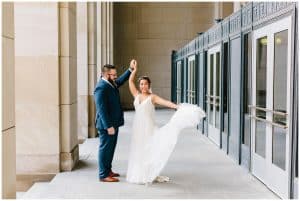 Wedding photo taken of a couple underneath a beautiful building in Grand Rapids as the groom twirls his bride.