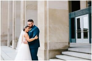 A bride and groom hug by some stairs as they prepare for their wedding ceremony.