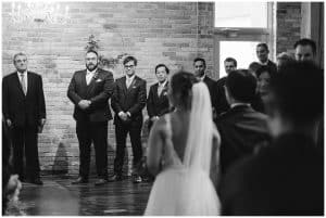 A photograph of the bride and groom standing in front of the officiant at their wedding ceremony.
