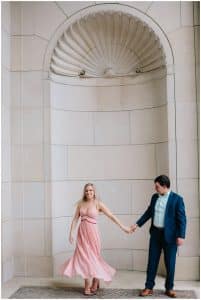 A couple dances under some arches at the U of M campus to avoid the rain during their engagement photo session with Mae Photo Co.