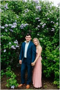 A couple stands in front of a blooming bush on the U of M campus for their engagement photos taken by Mae Photo Co.