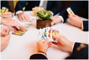 A groom sits at a table and plays cards with his groomsmen before the wedding.